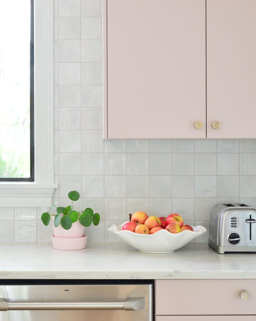 Square Tile Backsplash With Mauve Pink Painted Cabinets And Fruit Bowl