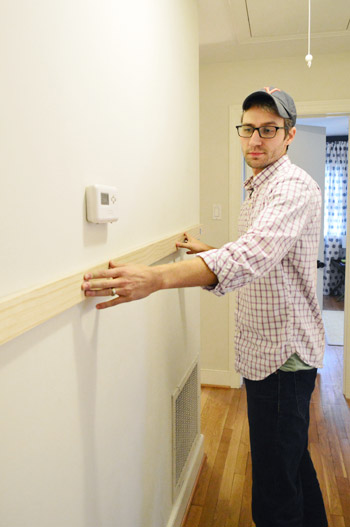 DIYer holding up wood board in hallway to determine height of board & batten project