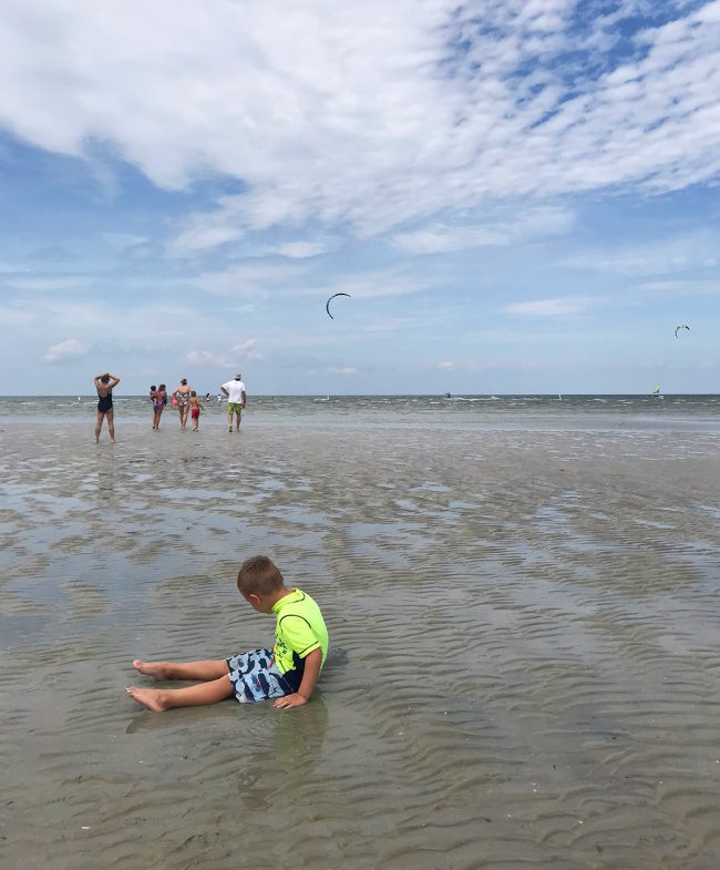 child sitting in shallow and with kiteboarders at cape charles beach
