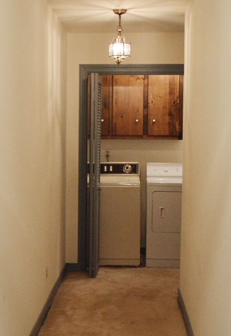 Dated laundry room closet at end of a hall with bifold doors, dark cabinets, carpet, and mismatched old washer and dryer