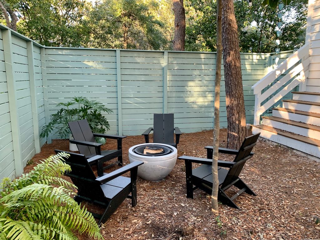 Painted fenced side yard with black Adirondack chairs around fire pit with potted plants