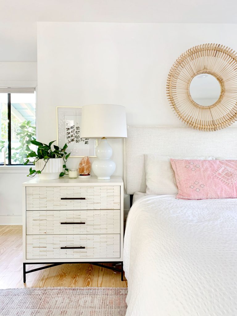 Linen headboard on bed with white bedding and inlay dresser as nightstand