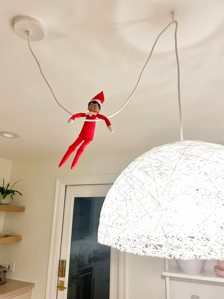 Elf on the Shelf hanging from pendant light cord in kitchen