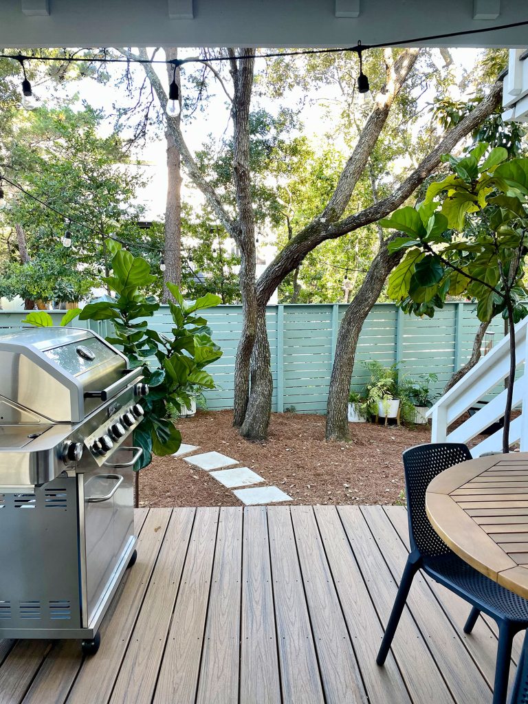 Vertical view from cover patio with grill and table overlooking greenery in yard