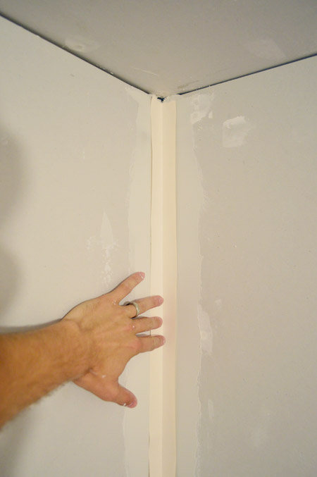 handing pressing drywall tape into corner layer of mud