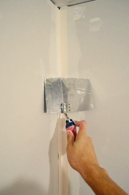 corner trowel pressing tape into corner of drywalled room