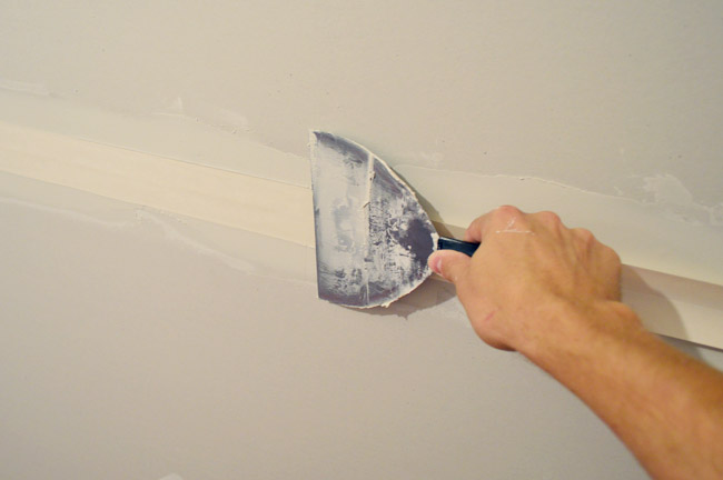 drywall knife smoothing tape into drywall tape and bottom layer of mud