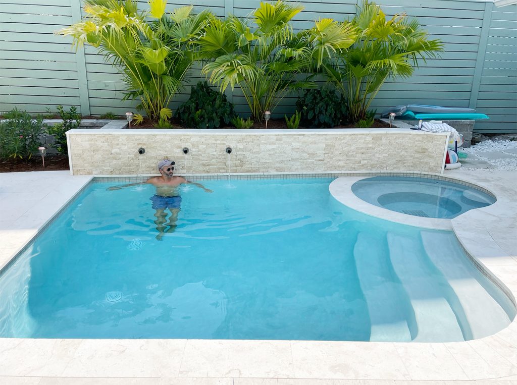 John in small freeform pool against stone accent retaining wall under palm plants